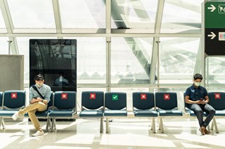 two people sitting on chairs at an airport while social distancing and wearing masks
