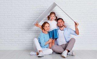 smiling family sitting under roof made from card