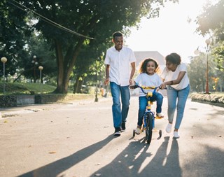 man and woman helping a girl to ride a bike