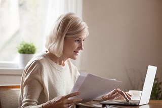 retired woman working on laptop holding documents