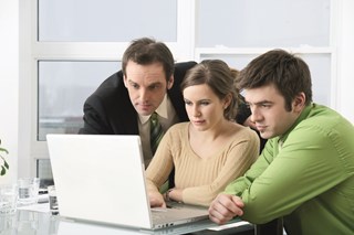 two men and one woman looking at a laptop