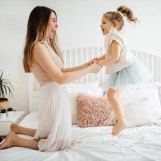 a mother holding her daughters hand while she jumps on top of a bed